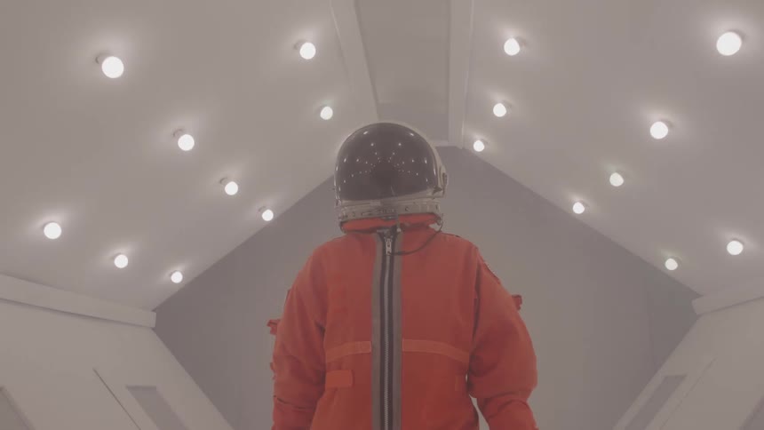 A person wearing a spacesuit and a helmet is standing in a brightly lit futuristic corridor the lighting creates a strong contrast silhouetting the person as they look straight ahead