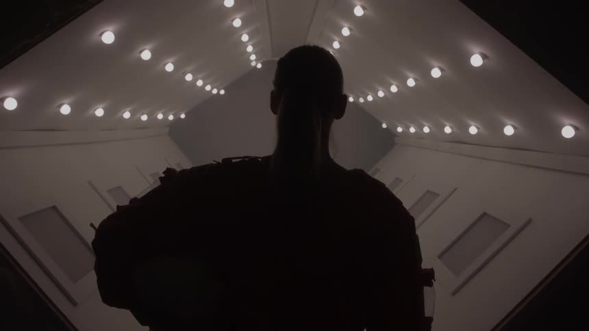Silhouette of a person in a spacesuit looking down a lit corridor