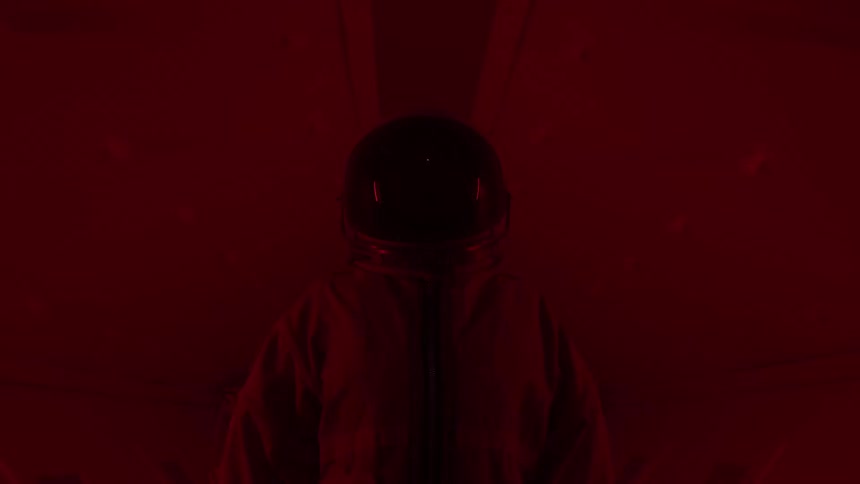 Astronaut in orange suit stands in corridor lit by red light