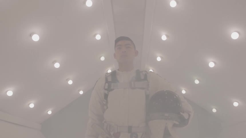 Young man walking inside a spaceship wearing a white spacesuit and holding a helmet in one hand