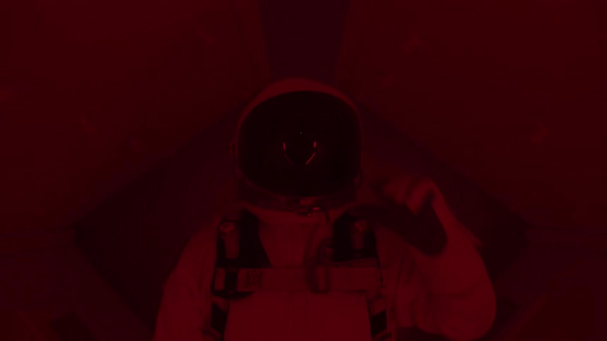 Astronaut adjusts helmet under intense red lighting