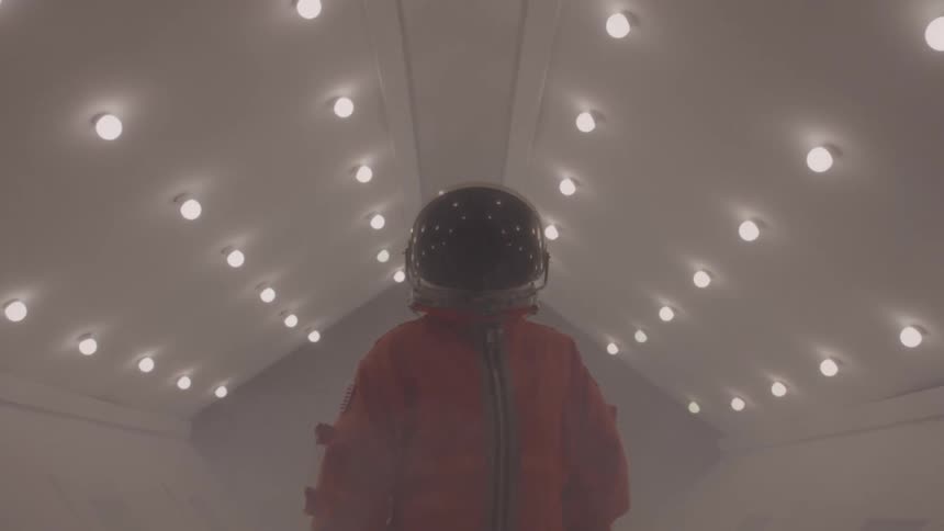 Astronaut in orange suit walks through corridor filled with mist and lights