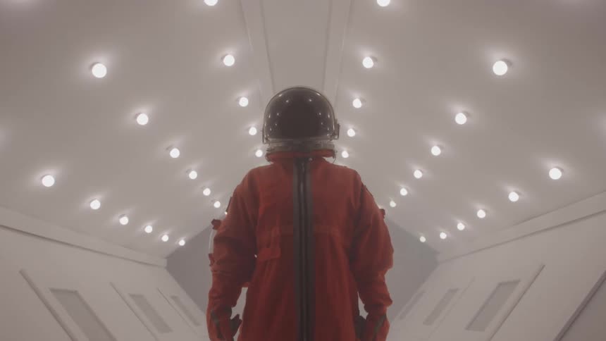 Astronaut in orange suit stands in illuminated corridor