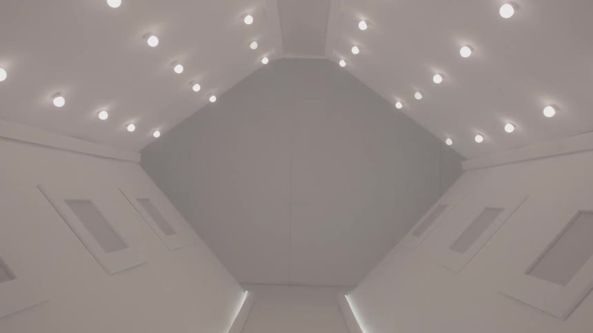 The interior of a clean futuristic white hallway with symmetrical lighting and panels is shown