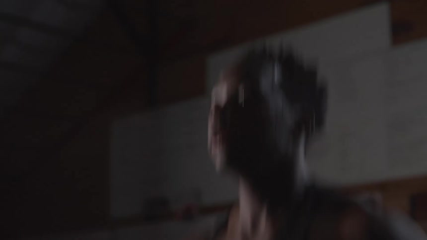 A man wearing a black tank top and sweating heavily jumps rope in a dimly lit gym