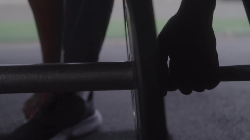 A close view shows a mans hands gripping a metal bar as he stands on a track wearing dark pants and sneakers