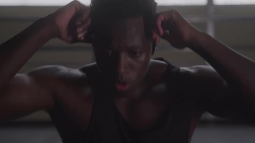 A close low angle view of a sweaty shirtless man doing a sit up in a gym with his hands behind his head