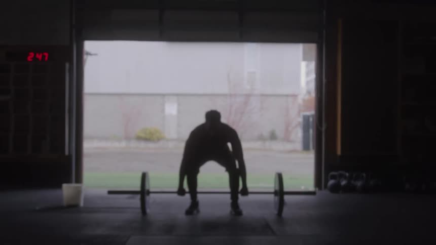 A young black male lifts gym weights in a fitness session indoors during daytime
