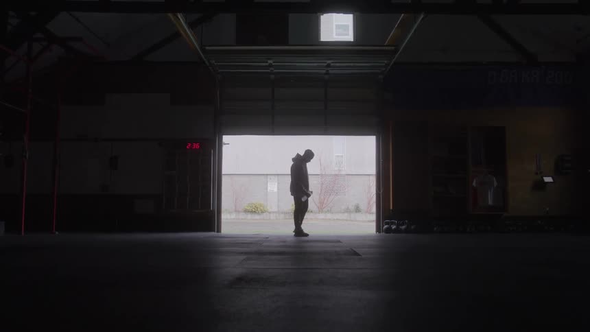 Silhouette of a young man drinking a bottle of water while standing at the entrance of a fitness room during daytime