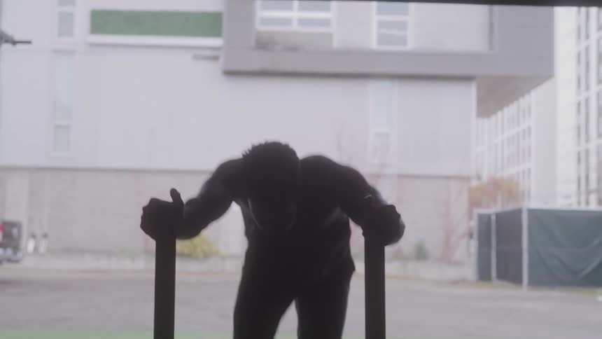 A muscular man is silhouetted as he pushes a weighted sled into a dark gym
