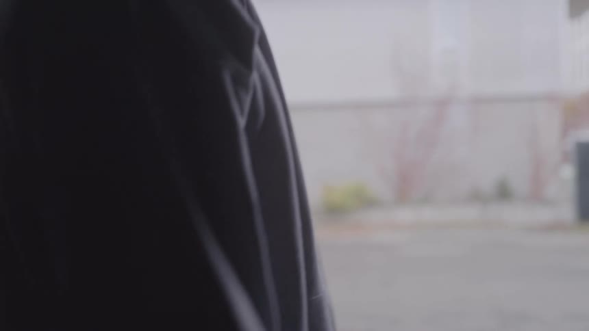 A silhouette of a man in a hoodie is shown from the side as he drinks from a clear water bottle with an urban building in the background