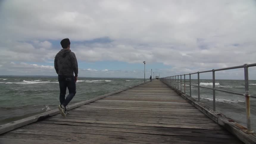 Man walking down a pier on a cloudy day