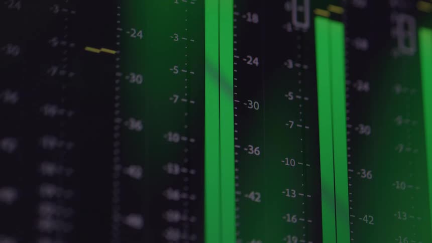 The video displays an abstract closeup shot of an audio equalizer with multiple vertical bars the bars rise and fall in a rhythmic motion glowing with a bright green light against a dark background simulating audio levels in a recording studio