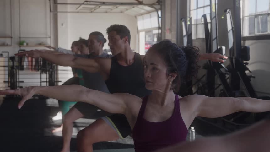 Yoga group of young males and females lined up in a gym at midday stretching with hands spread apart