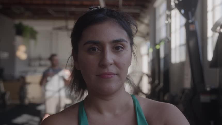A woman stands in soft natural light inside a spacious gym
