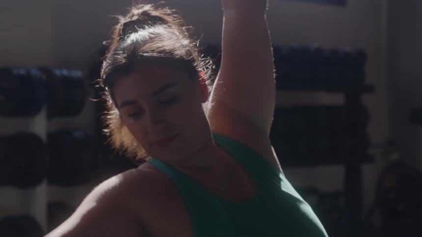 A woman stretches with one arm raised inside a gym