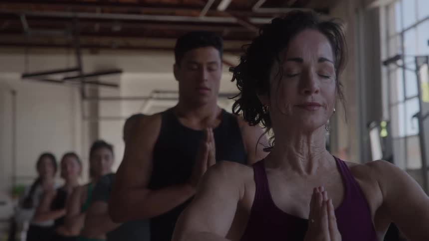 Group of young men and women meditating in yoga pose inside a gym