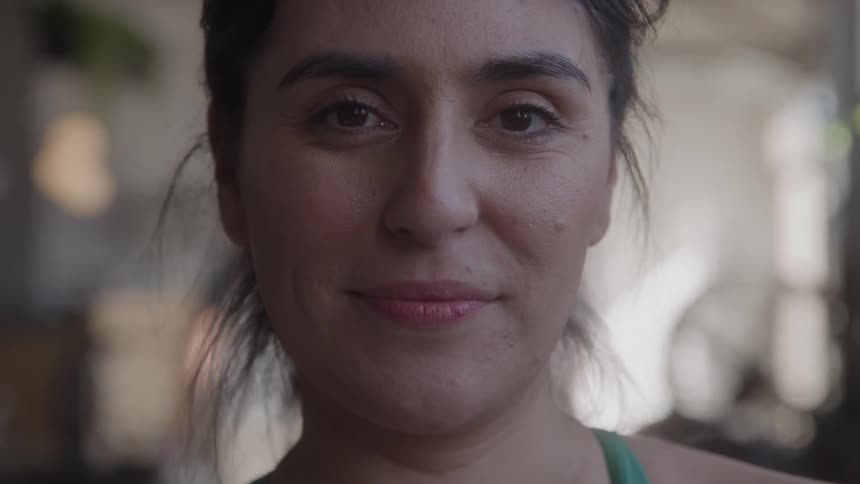 A close view of a smiling woman with her hair in a bun looking at the camera in a gym setting