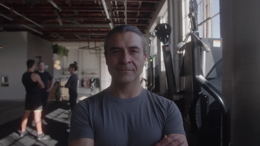 Middleaged man in a gym after a yoga session with three other people in the background engaged in a discussion