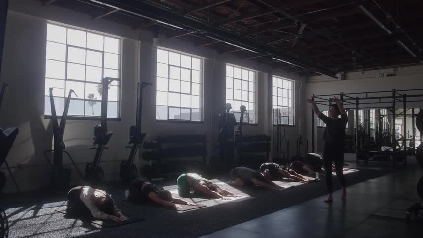 Female yoga instructor walks past her students as they stretch during a yoga class at a gym