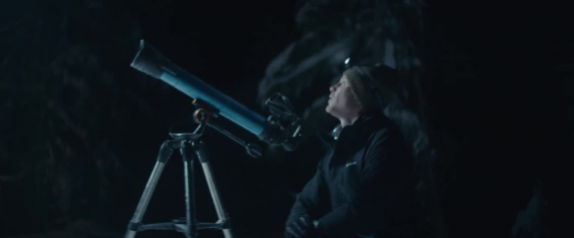 The video shows a person at night outdoors looking through a telescope the person is wearing a headlamp which illuminates their face as they look up from the telescope seemingly in awe