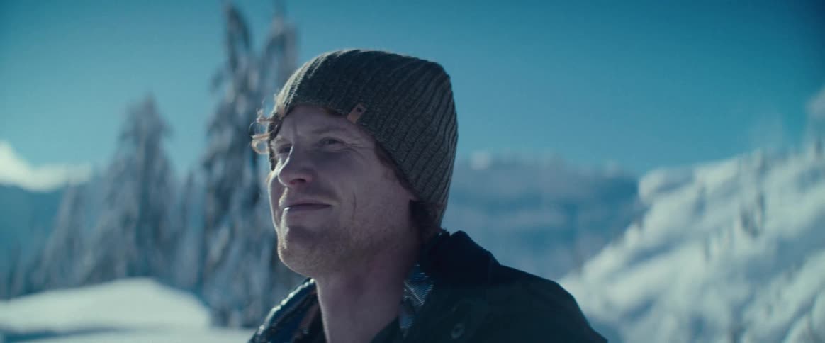 The video shows a man standing in a snowy mountainous environment he is wearing a beanie and a jacket and appears to be smiling and enjoying the view