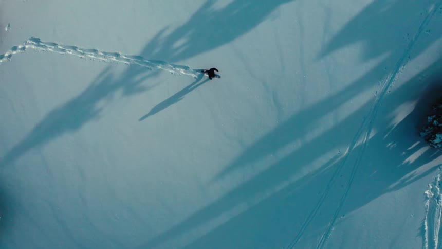 Person walking in the snow at midday leaving a trail of footprints behind