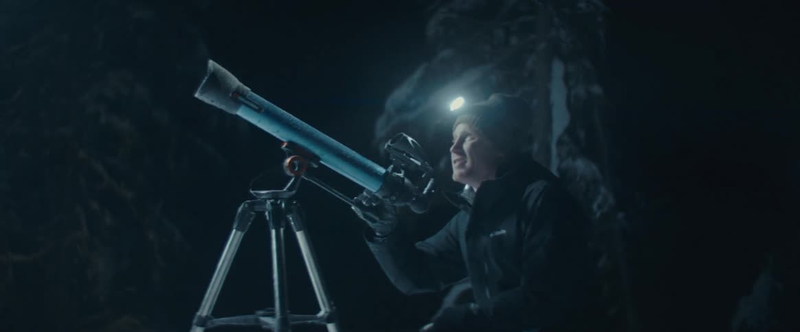 Person with a headlamp observes through a telescope at night