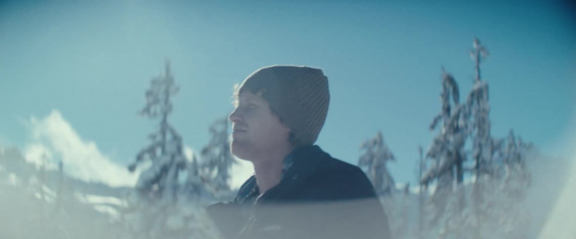 A camera focuses on a persons face as they look around in a snowcovered mountain landscape