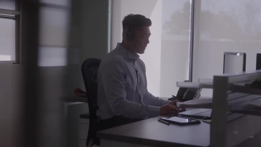 Man wearing headphones works on the computer while holding documents