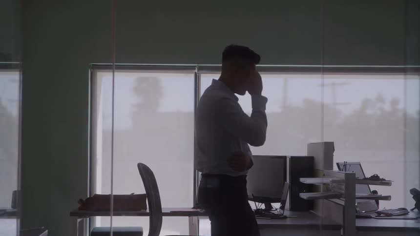 The man walks in the office while talking on his phone