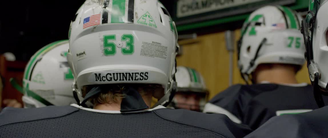 The video shows a group of american football players in a locker room getting ready for a game they are wearing their jerseys and helmets and the helmet of a player in the foreground has the name mcguinness and the number 53 on it