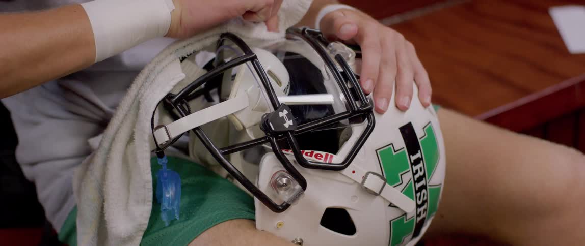 The video shows a group of american football players in their locker room two of the players are sitting at a table with their backs to the camera wearing black and green jerseys