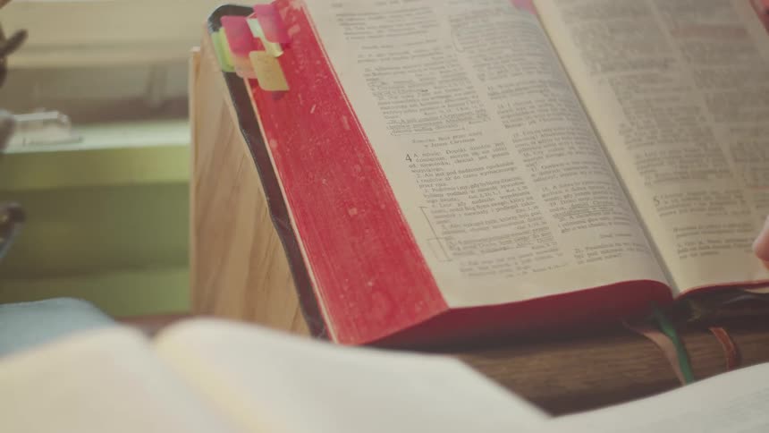 Persons hand opening a bible page with the bible placed on a desk