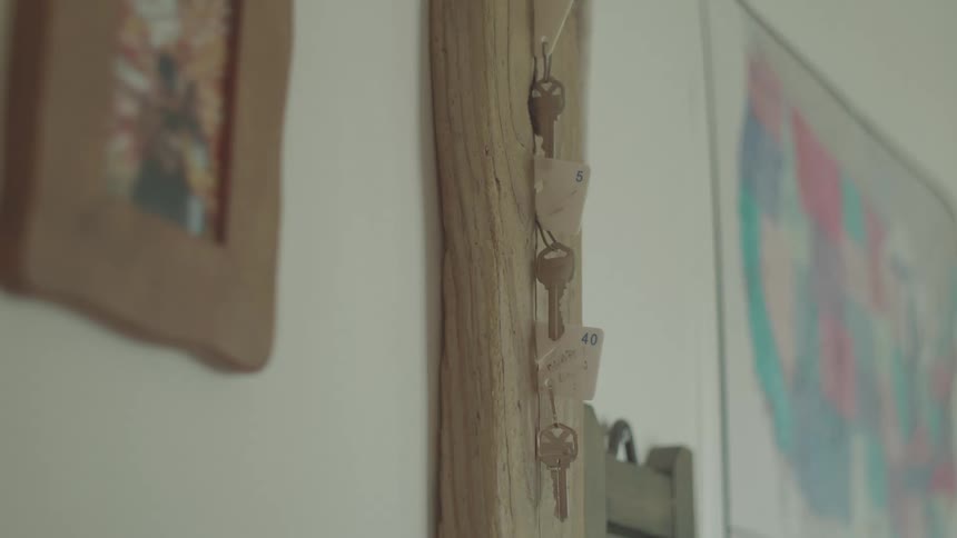 Several keys with numbered tags hang from hooks on a wooden board with framed pictures blurred in the background