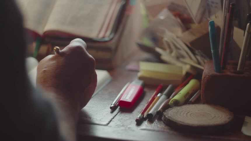 A close up on a man hand writing something on a book over a table in an indoor setting
