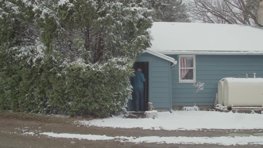 Elderly man walking into a basement from outdoors wearing a winter jacket in snowy weather