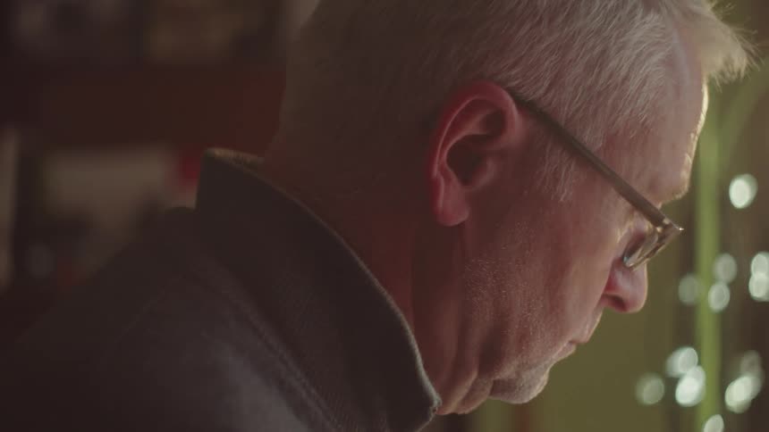 Older man in warm light looking down thoughtfully