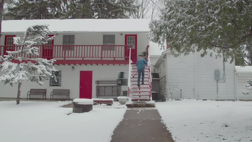Man climbs red stairs of a snowcovered house and sweeps with a broom