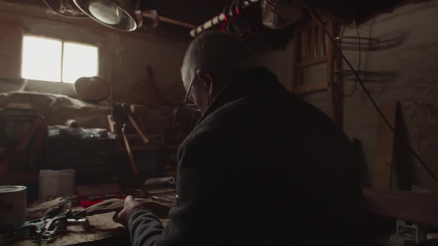 Elderly man sitting in his makeshift workshop in a garage focused on his work