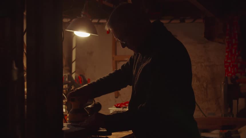 The man is sanding wood in the workshop