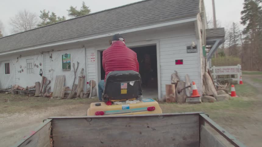 A man rides a lawnmower with a trailer in a yard near a house