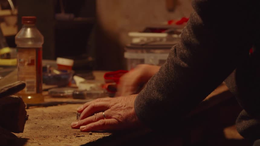 Hands of an elderly person working on a wooden workbench