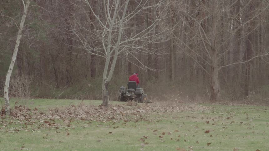 The man rides the lawnmower and cops up the leaves