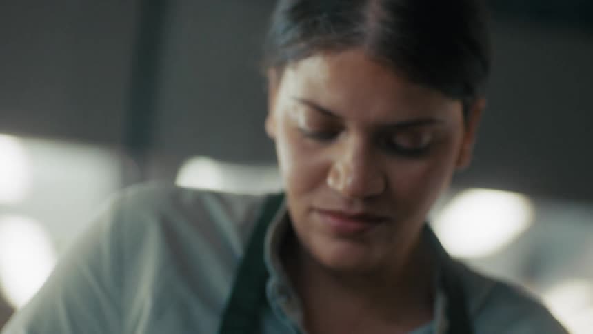 Woman wearing a green apron looks down focused