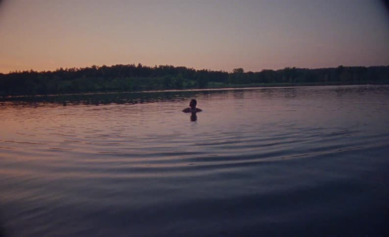 Person swims in a lake at sunset with trees in the background