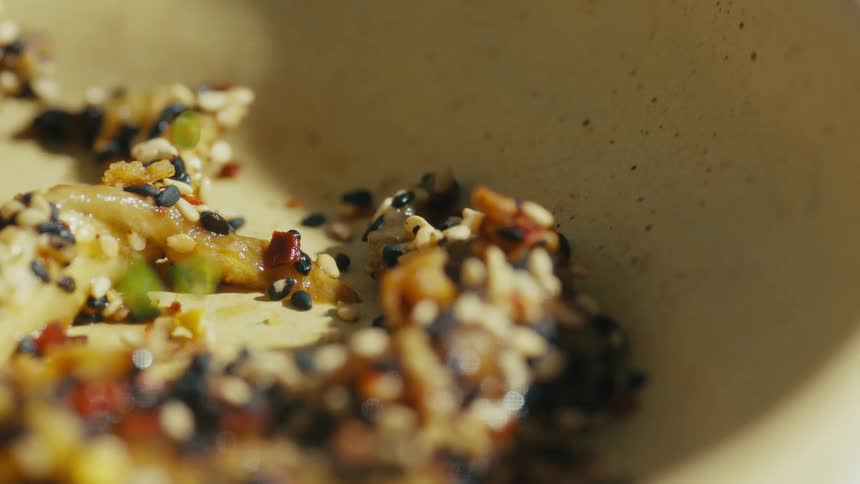 The video shows a closeup shot of a white bowl filled with what appears to be fried vegetables covered in sesame seeds the camera slowly pans out to reveal the bowl on a whitespeckled countertop