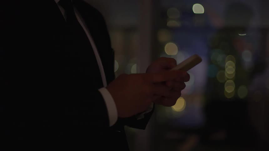 Man wearing a suit standing in the middle of the street at night using his phone under the glow of streetlights