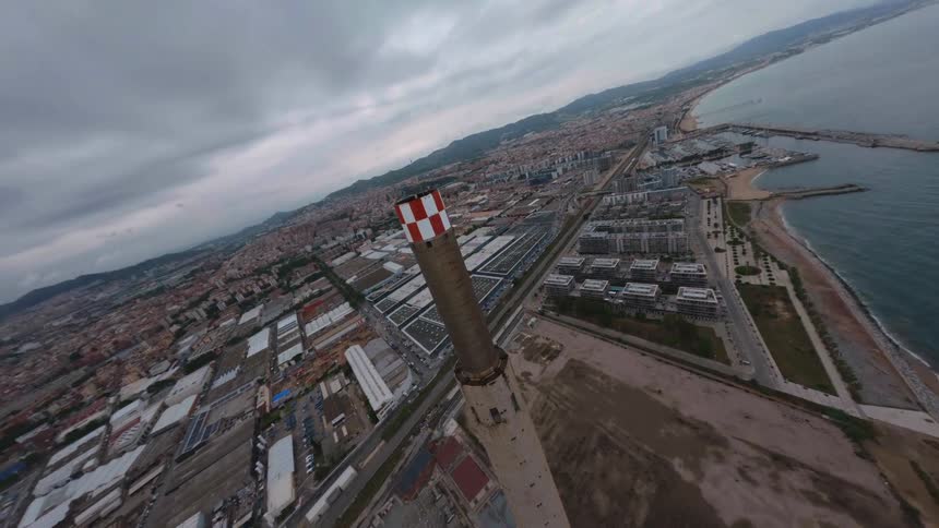 Three industrial chimneys in a factory on a coastline with the city skyline and ocean visible in the background at midday