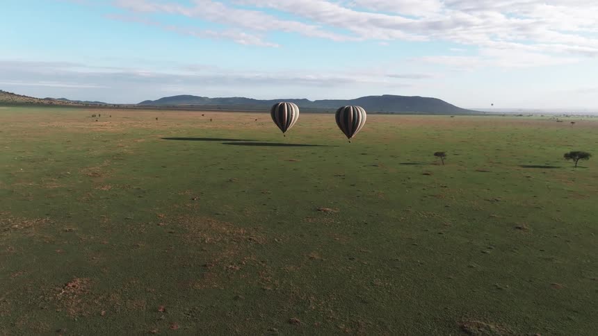 Two hot air balloons fly over land with mountains in the background